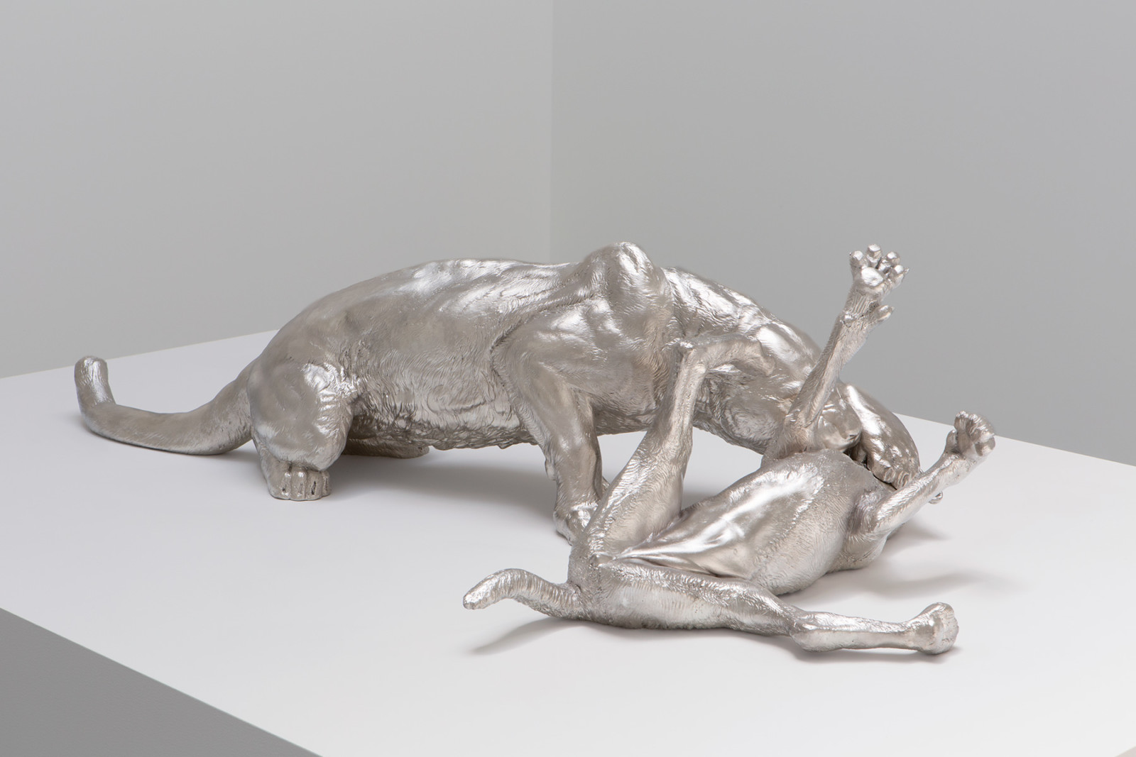 Large sculpture on white pedestal of a mountain lion that is hunched over with its muscles flexed as it bites down on a dog's neck