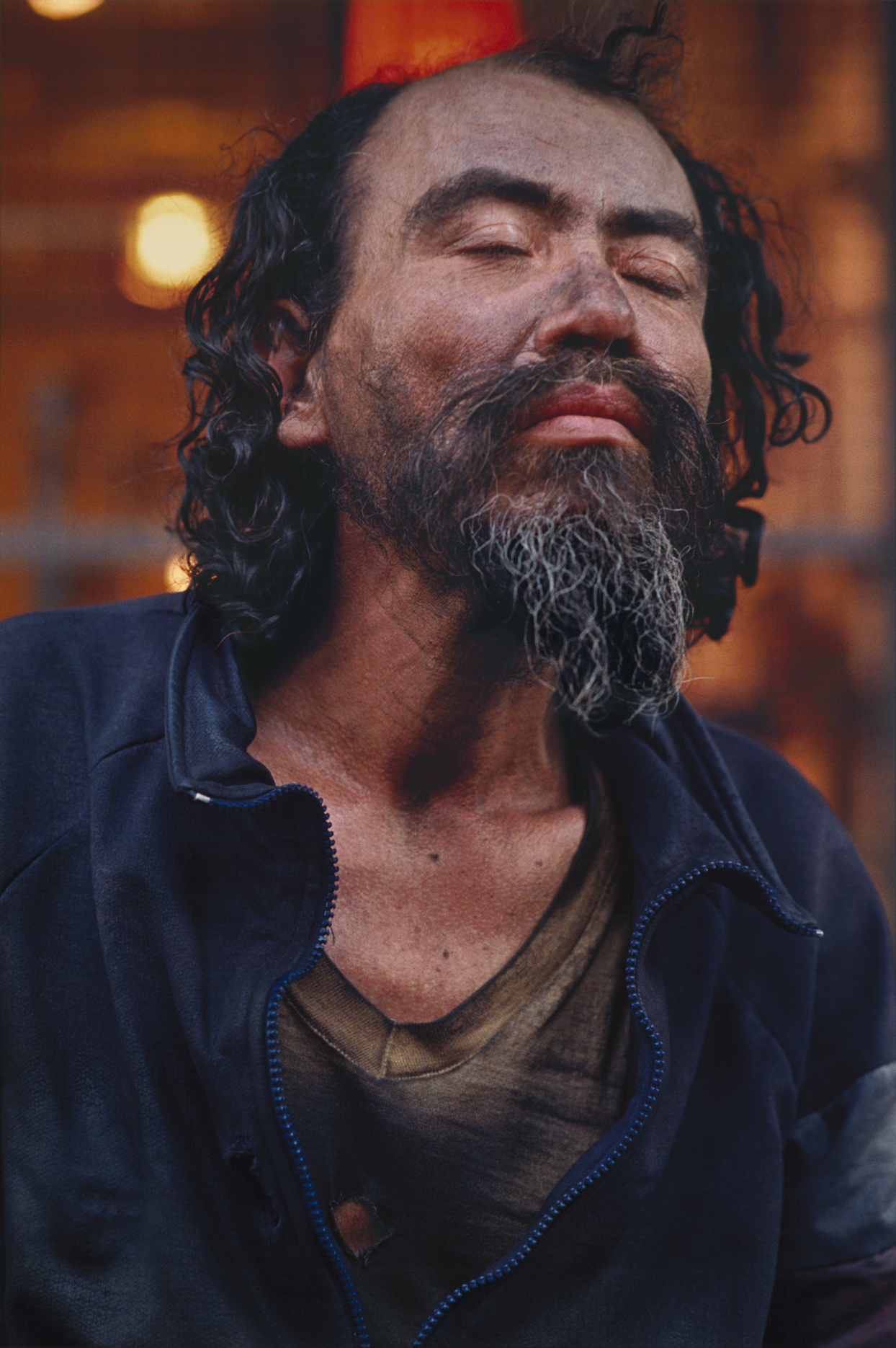 Portrait of a man with his eyes closed, face covered in soot, and a greying beard.