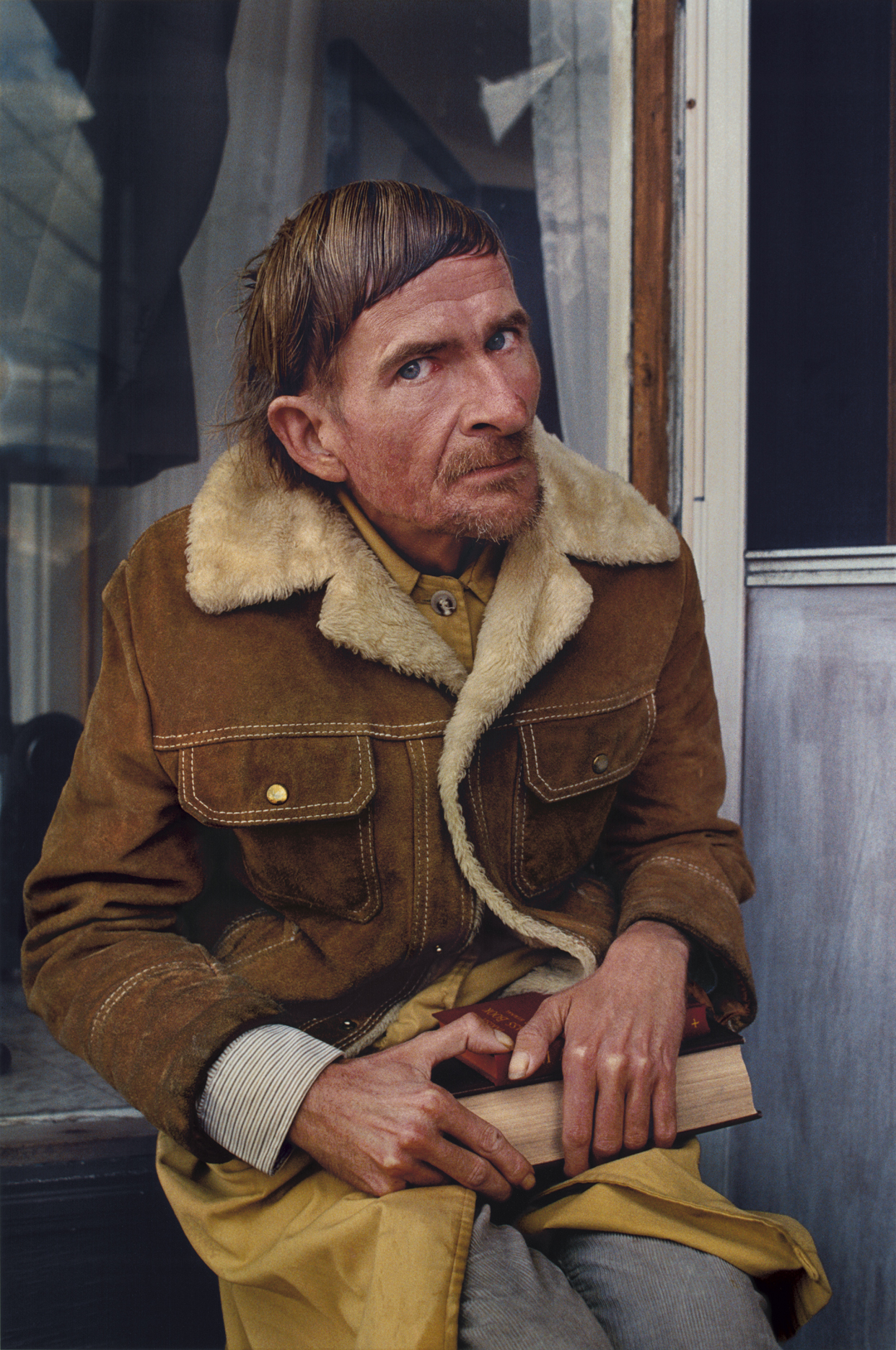 Photograph of a man in a shearling coat holding a piece of wood.