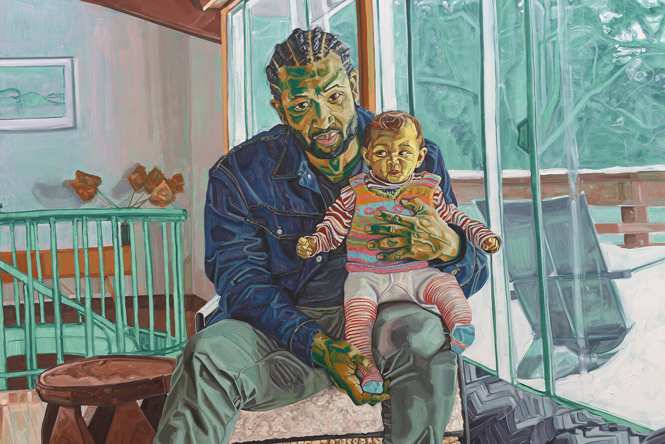 Man seated inside home with infant on his lap.